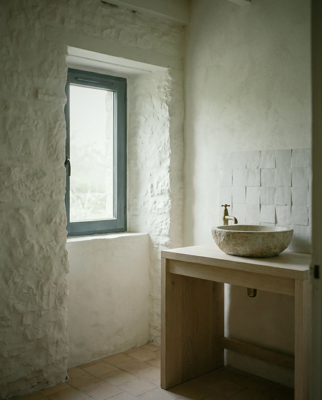 Salle d’eau du penty : carreaux blancs faits main, vasque en pierre sur plan de bois, robinet laiton, sol en tomettes.