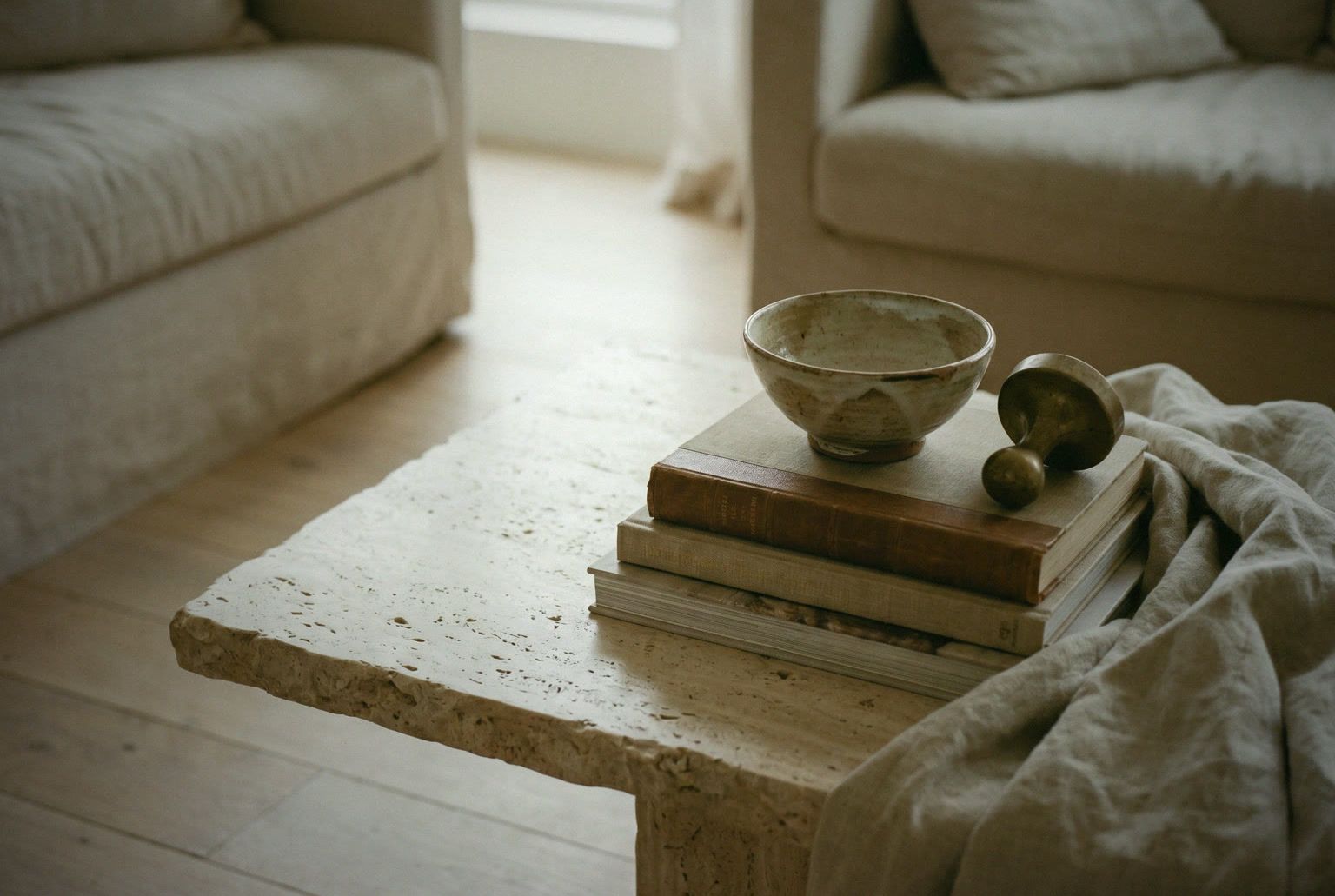 Détail : coin de table en travertin, livres et céramique, lumière sur le lin.