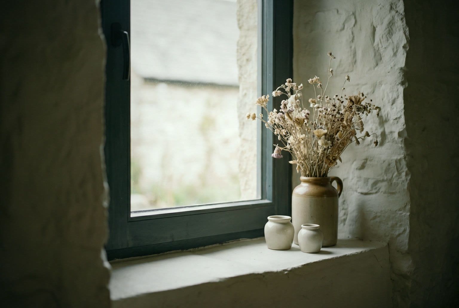 Détail : bouquet séché en pot de grès et céramiques sur l’embrasure de pierre chaulée, fenêtre ardoise.